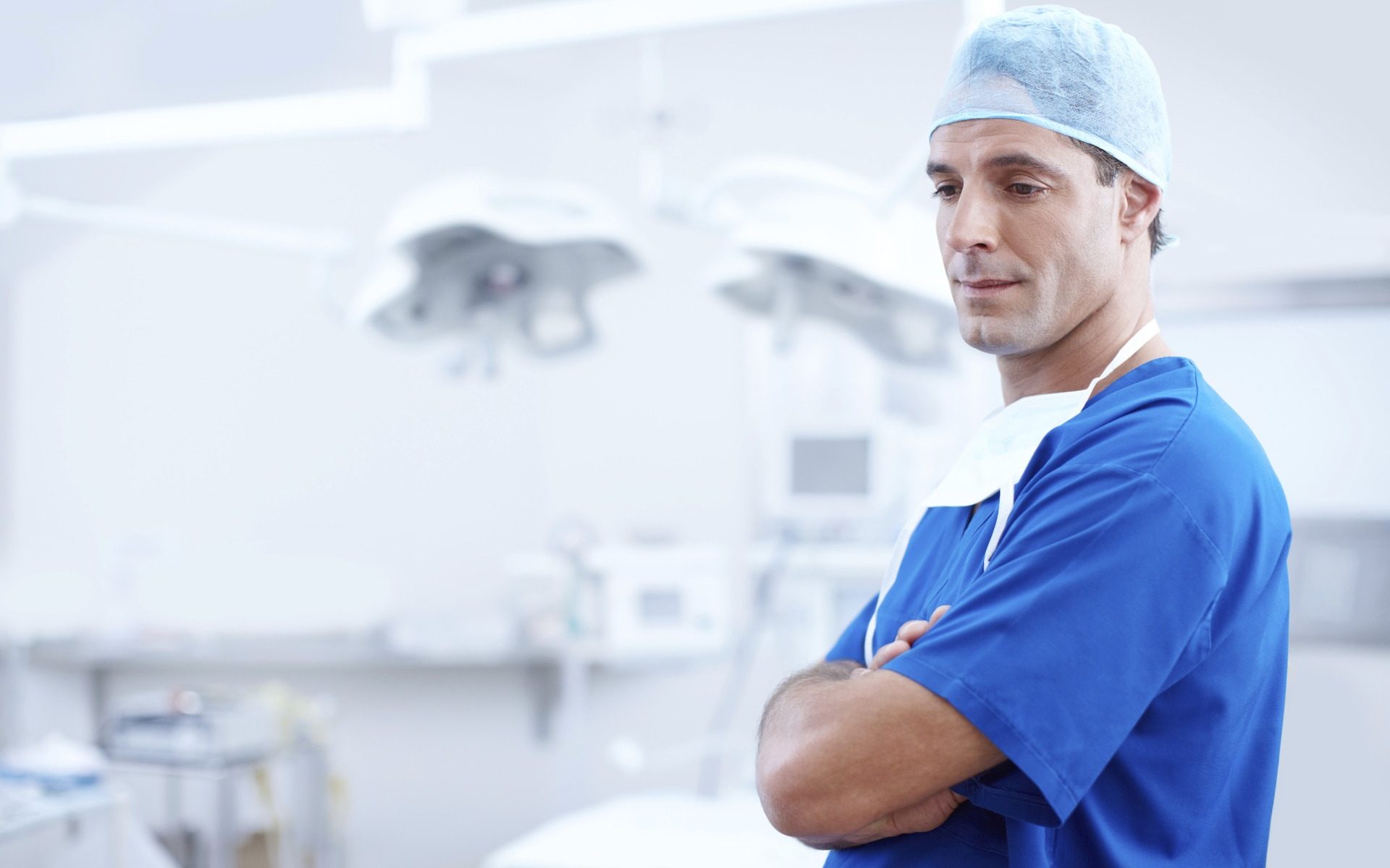 A surgeon standing in an operating room with his arms crossed.